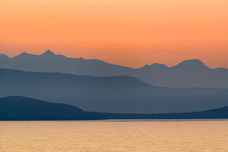 calm body of water near green tree mountains thumbnail