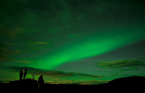 silhouette of three person standing on cliff under Aurora Borealis thumbnail
