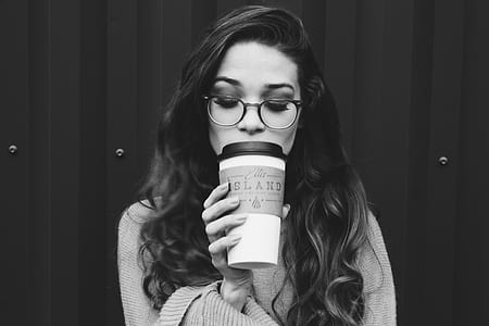 grayscale photography of woman holding cup standing beside wall thumbnail