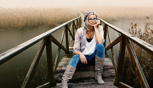 woman in white shirt with brown cardigan and brown boots sitting on brown wooden bridge during daytime thumbnail