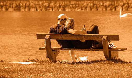 man and woman sitting on brown bench near body of water thumbnail