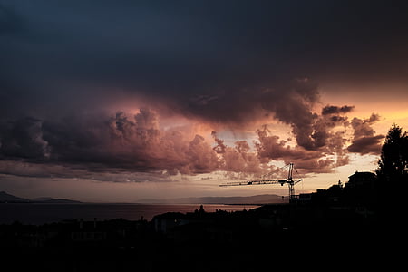 silhouette of tower crane under grey clouds during golden hour thumbnail