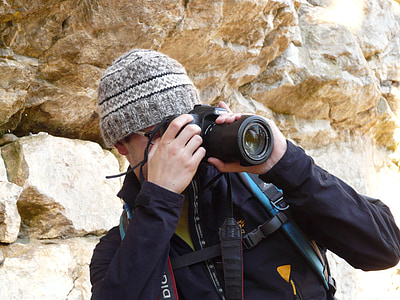 man capturing using DSLR camera behind rocks thumbnail