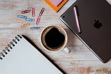 black liquid filled white ceramic mug between paper and iPad thumbnail
