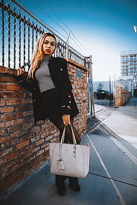 woman carrying tote bag while leaning on brick wall thumbnail
