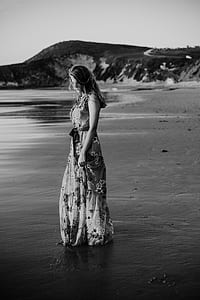 grayscale photo of woman standing near body of water thumbnail