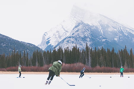 four people playing ice hockey on field near pine trees thumbnail