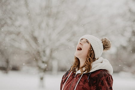 woman looking up in maroon hoodie standing on snow during daytime thumbnail