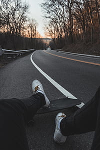 person sitting on asphalt road surrounded by bare trees thumbnail