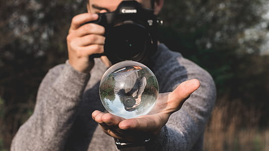 Man Wearing Space-dyed Sweater Holding Water Globe While Holding Black Canon Camera thumbnail