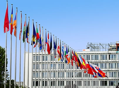 line of assorted-color flags beside white concrete building under blue sky at daytime thumbnail