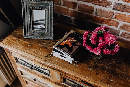 Photo frame, books and pink flowers in a vase on a wooden commode thumbnail