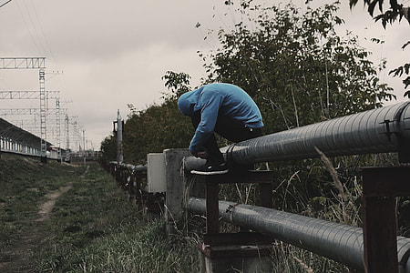 person sits on railing pipes near tall trees at daytime thumbnail