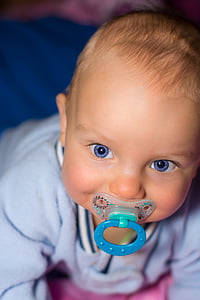 close up photo of baby biting blue pacifier thumbnail