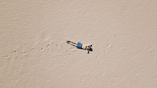 person lying on open white sand in aerial photography at daytime thumbnail