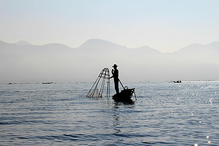 silhouette of man on boat in distant of mountain thumbnail