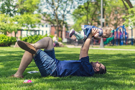 selective focus photography of man holding baby while lying on grass thumbnail