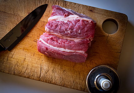 raw meat on brown wooden chopping board besides black kitchen knife thumbnail
