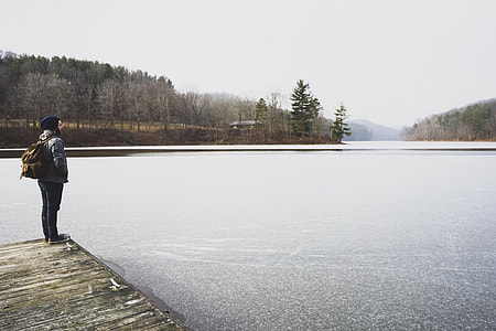 photo of person standing on dock facing body of water thumbnail