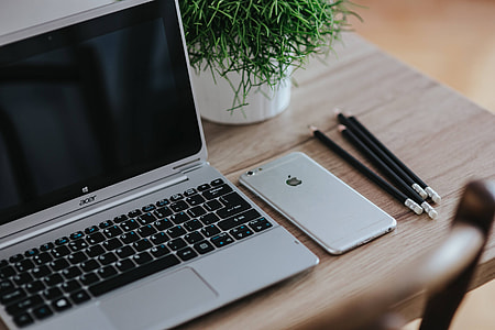 Silver Acer laptop on a wooden desk with a green plant, pencils and an Apple iPhone thumbnail
