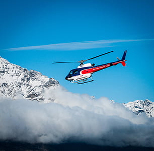 white, blue, and red helicopter hovering on snow-covered mountain during daytime thumbnail