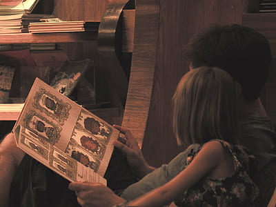 man holding storybook near girl leaning on sofa thumbnail