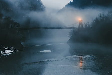 lighthouse near bridge over body of water in mist thumbnail