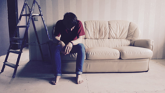 man sitting on brown couch beside black A-type ladder thumbnail