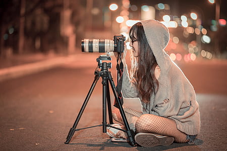 woman in grey hooded jacket sits on road using DSLR camera with tripod thumbnail