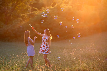 two women wearing mini dresses playing bubbles on grass field thumbnail