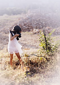 girl wearing white dress taking a photo to the brown grass thumbnail