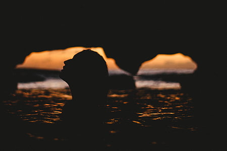 silhoutte photography of person on body of water under cave thumbnail