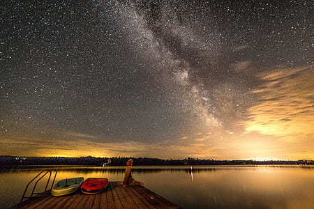 person sitting on brown wooden dock at night time thumbnail