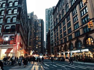 people walking on sidewalks and crossing street surrounded by buildings thumbnail