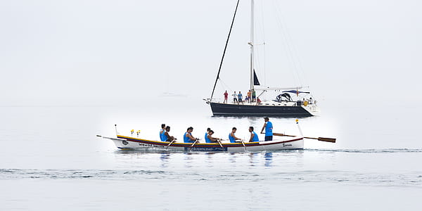 people riding white and brown canoe near white and black sailboat thumbnail