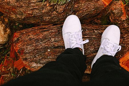 person wearing black pants and white sneakers standing on wood log thumbnail