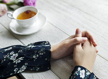 woman's hand near white ceramic teacup and saucer on brown wooden table thumbnail