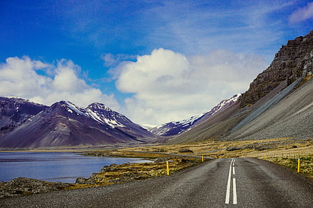 concrete road with no vehicles beside body of water under white and blue sky at daytime thumbnail