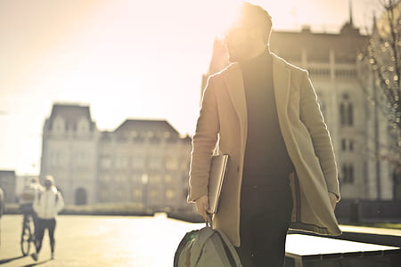 person wearing gray coat, holding laptop and bag while looking at his left thumbnail