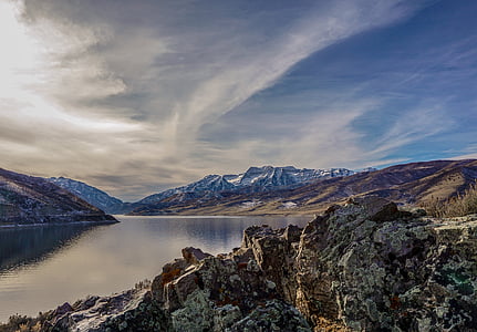 landmark photo of body of water across mountains under white and blue cloudy skies thumbnail