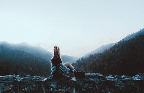 woman sitting on rock while looking at mountain thumbnail