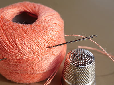 silver thimble beside orange thread with needle thumbnail