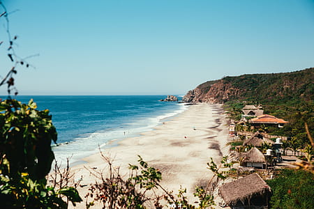 Dry grass rooftops at a beach resort in with blue ocean in the foreground thumbnail
