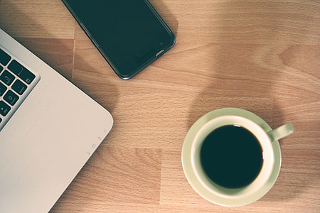 white ceramic mug full of black coffee near laptop and smartphone thumbnail