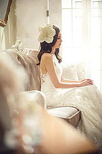 woman in white sleeveless floral wedding gown sitting on brown couch thumbnail