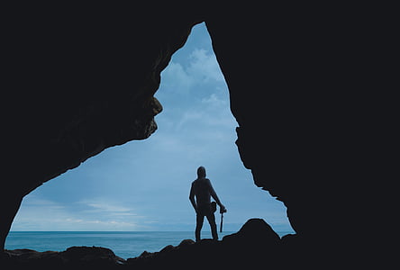 silhouette of person standing inside cave near sea thumbnail