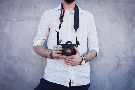 man holding camera leaning on wall thumbnail