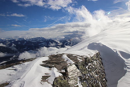 aerial photography of snow covered mountain overlooking hills under white and blue cloudy skies at daytime thumbnail