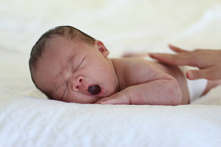 yawning baby lying on white textile thumbnail
