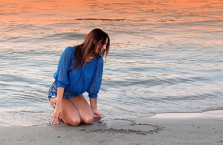 woman in blue elbow sleeved shirt kneeling on beach during sunset thumbnail